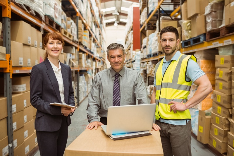 Smiling warehouse team working together on laptop